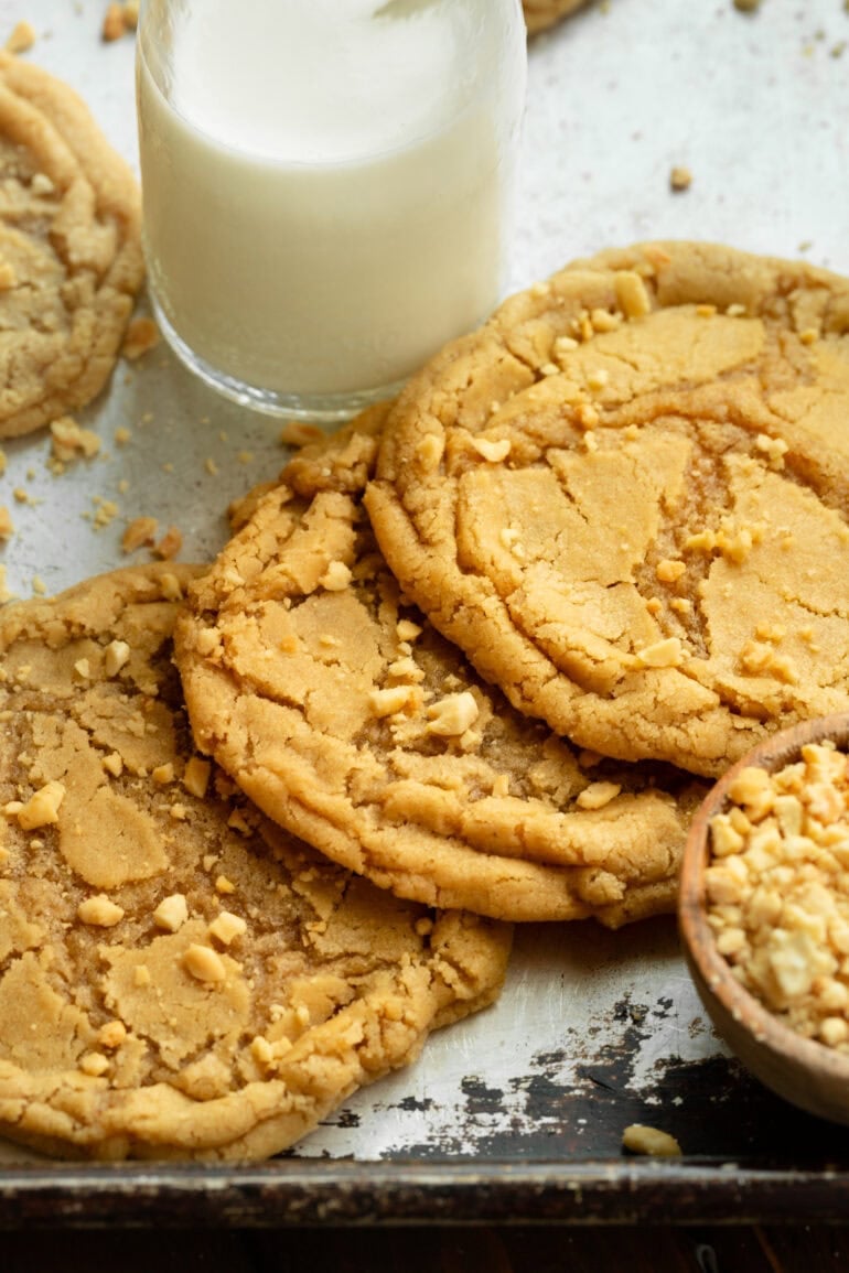 Photo of several large chewy peanut butter cookies sitting in front of a tall glass of milk