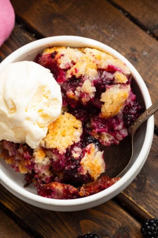a photo of a bowl of blackberry cobbler topped with a scoop of vanilla ice cream