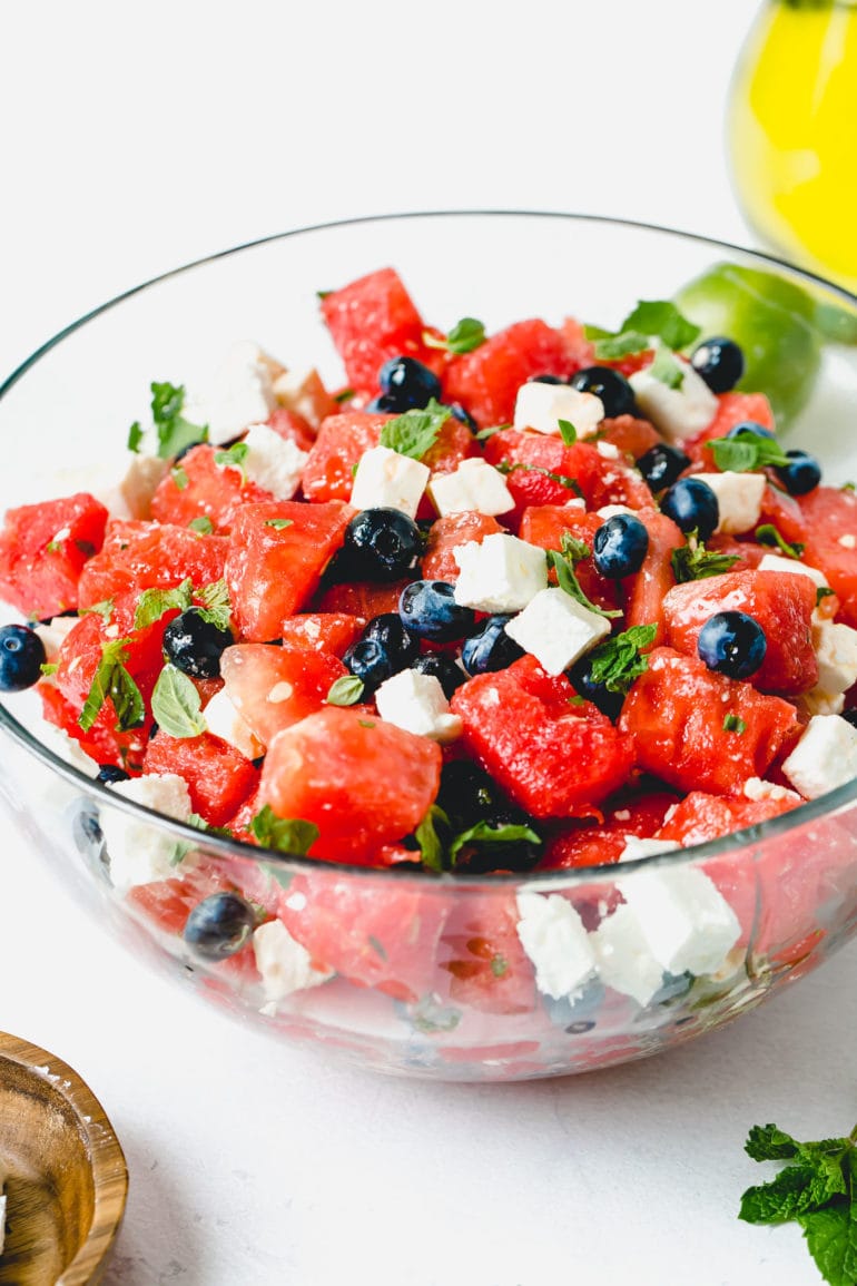 A blueberry feta watermelon salad with cubes of feta cheese and fresh basil and mint leaves.
