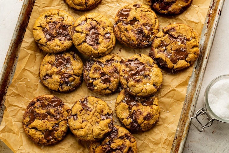 a cookie sheet with parchment is topped with Brown Butter Chewy Pumpkin Chocolate Chip Cookies topped with flaky salt