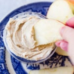 a blue dish holding a sliced apple and half of an apple with a small dish of healthy peanut butter greek yogurt dip