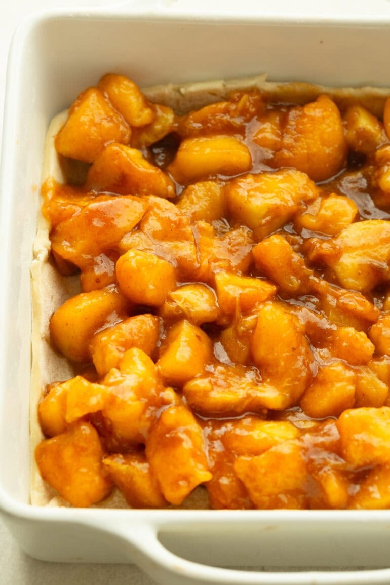 Close-up of baked peach filling in a white baking dish, showing soft, juicy peach chunks coated in a glossy cinnamon-sugar sauce.