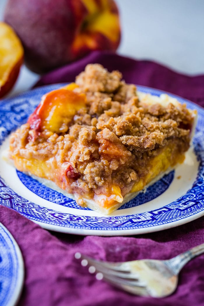 A purple napkin under a vibrant blue china designed dessert plate with a slice of brown sugar peach pie bars