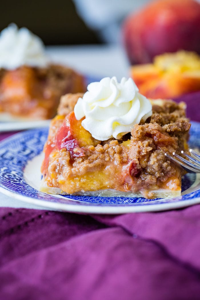 A purple napkin under a vibrant blue china designed dessert plate with a slice of brown sugar peach pie bars