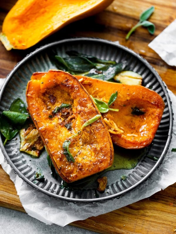 a photo of two halves of a honeynut squash face up and golden brown with fresh sage leaves on top.