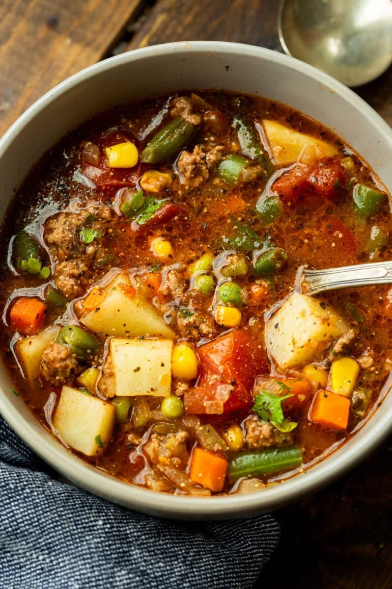 a bowl of ground beef vegetable soup with a spoon sitting in the bowl