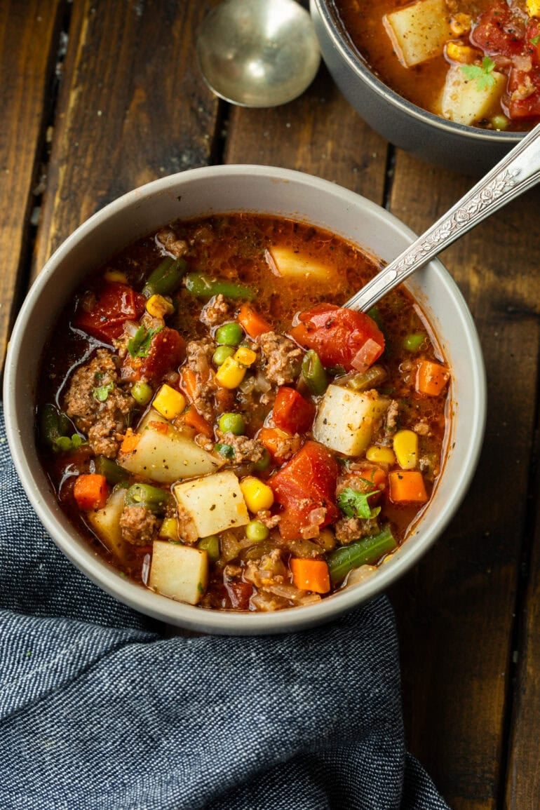 a bowl full of ground beef vegetable soup with a spoon in the bowl