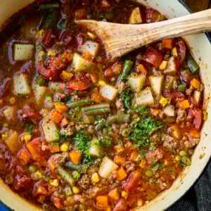 a large bot of ground beef vegetable soup topped with minced fresh parsley with a wooden spoon in the bowl