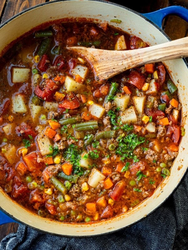 a large bot of ground beef vegetable soup topped with minced fresh parsley with a wooden spoon in the bowl