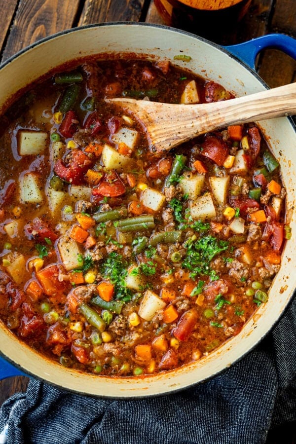 a large bot of ground beef vegetable soup topped with minced fresh parsley with a wooden spoon in the bowl