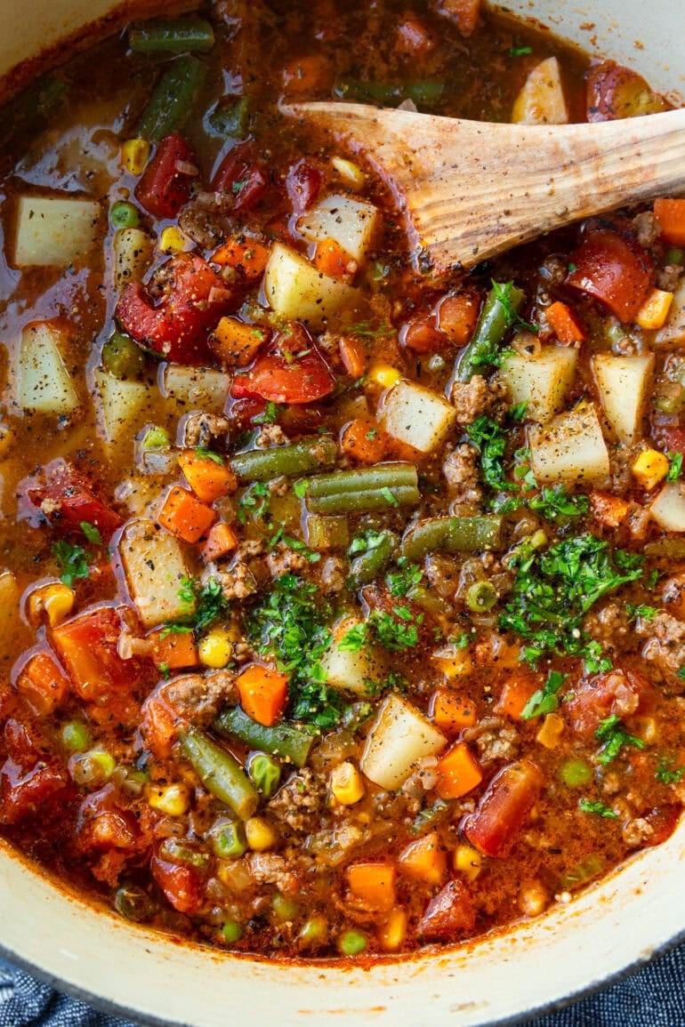 a wooden spoon stirring a pot of ground beef vegetable soup