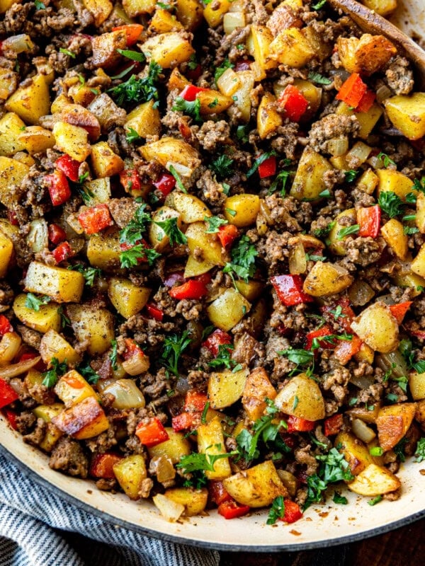 a photo of a cast iron skillet full of crispy potatoes and ground beef mixed with onions and red bell peppers