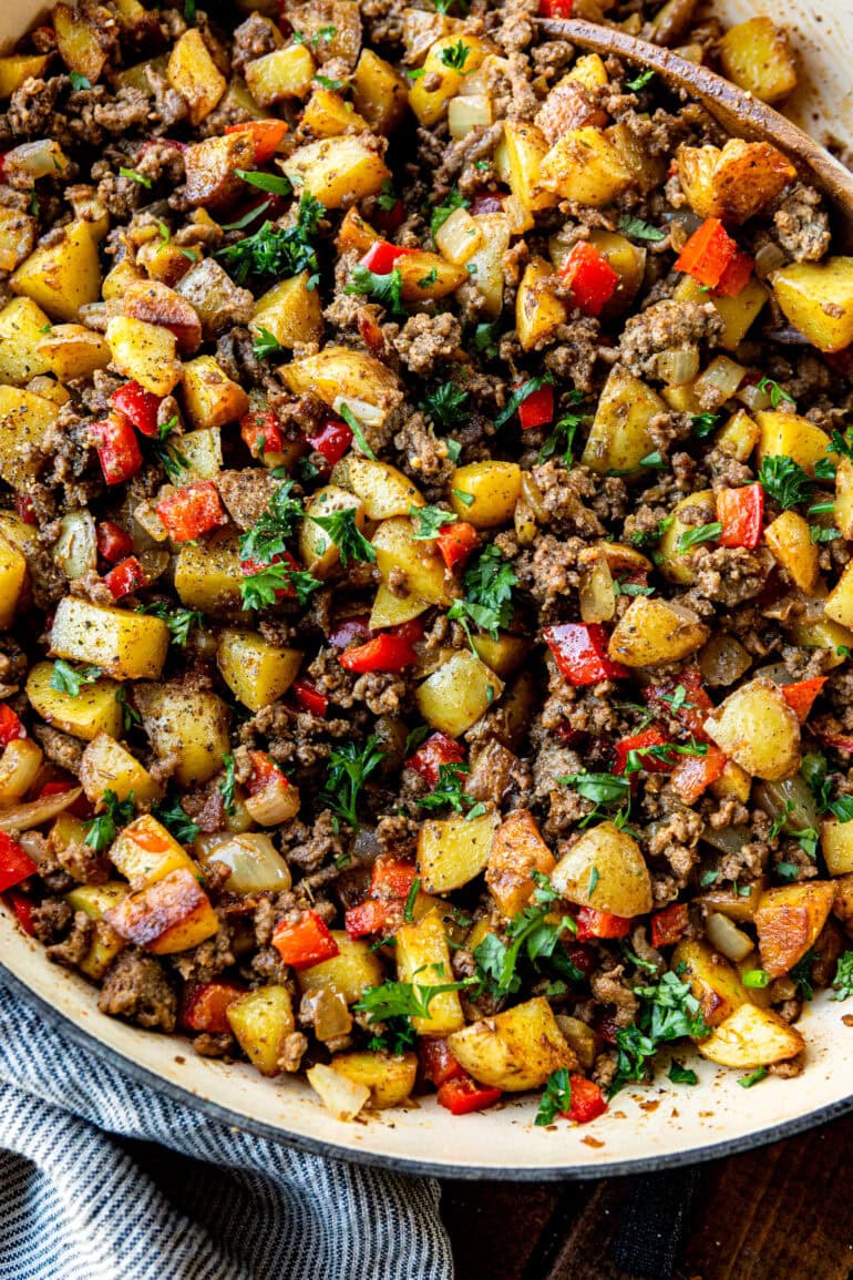 a photo of a cast iron skillet full of crispy potatoes and ground beef mixed with onions and red bell peppers
