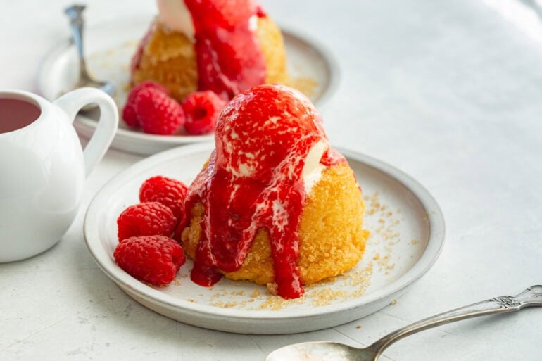 a small dessert plate with an individual gooey butter cake topped with vanilla ice cream and fresh raspberry sauce