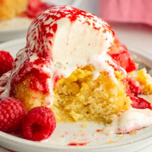 an individual gooey butter cake topped with a scoop of vanilla ice cream and fresh raspberry sauce