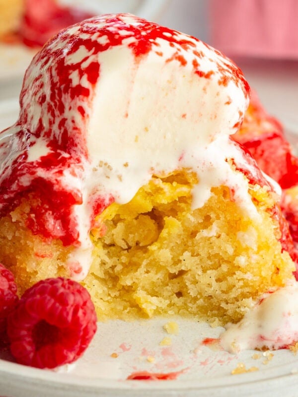 an individual gooey butter cake topped with a scoop of vanilla ice cream and fresh raspberry sauce