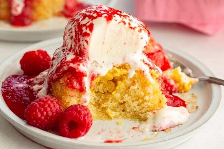 an individual gooey butter cake topped with a scoop of vanilla ice cream and fresh raspberry sauce
