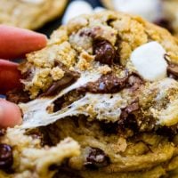 a black background with a stack of s'mores chocolate chip cookies being broken apart with marshmallow stretching out.