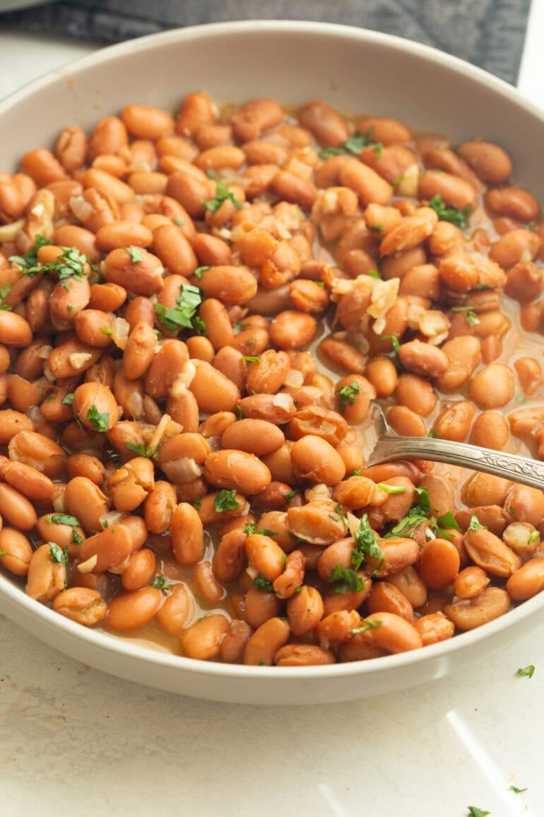 a bowl full of seasoned pinto beans with a spoon lifting a serving of the beans