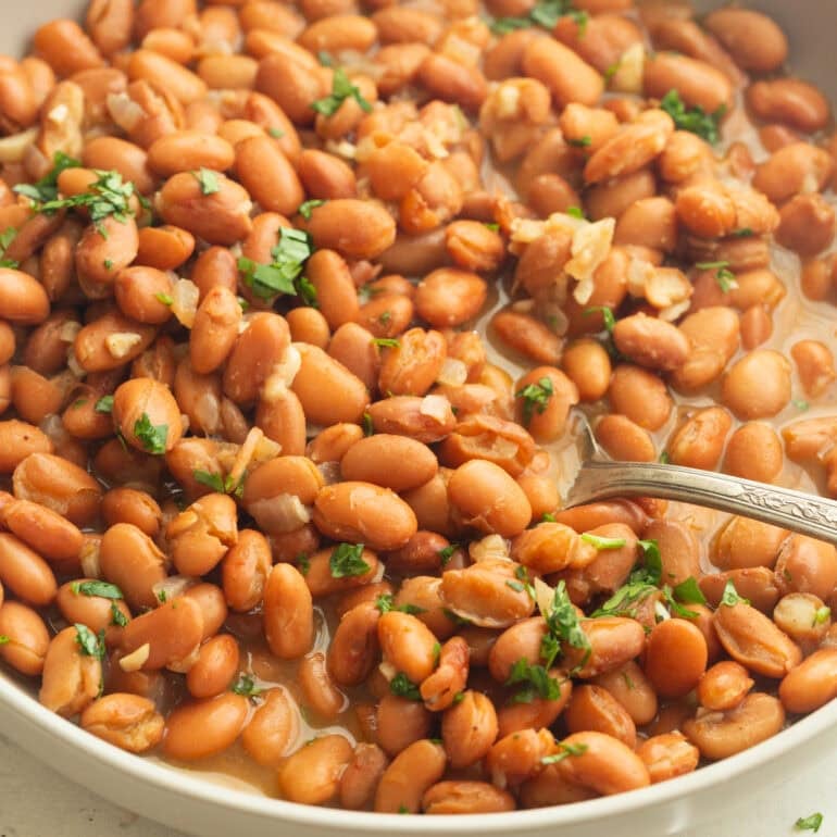 a spoon lifting a serving of seasoned pinto beans from a full bowl of the beans