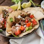Two authentic carne asada tacos on a serving plate on top of a wooden table.