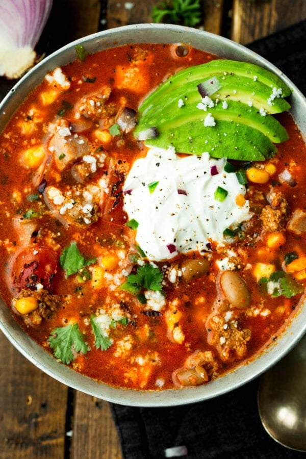 a bowl of charro bean soup topped with sour cream and sliced avocados