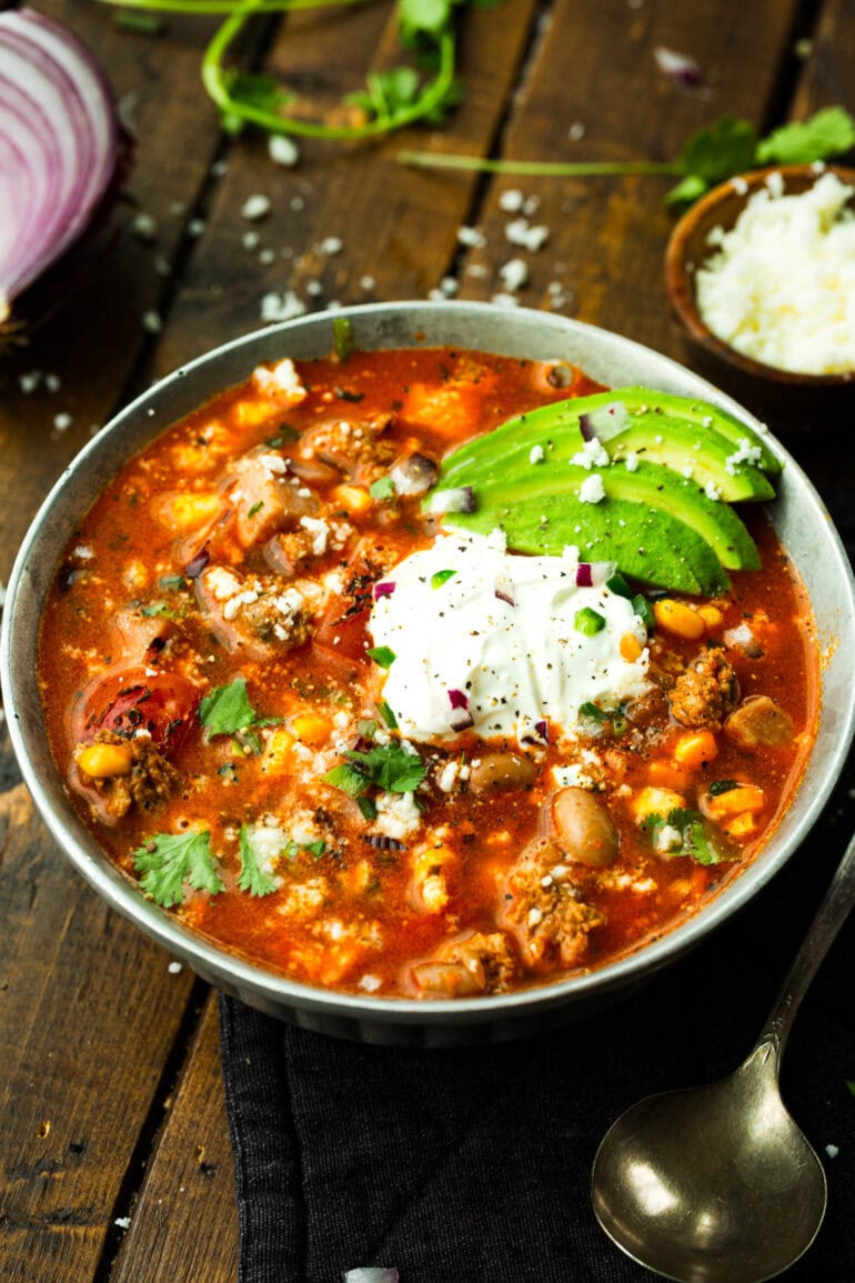 a bowl of hearty charro bean soup topped with sour cream, sliced avocados and sprinkled with chopped cilantro