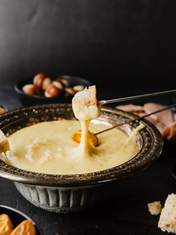 A skewer of bread that has been dipped in cheese fondue. the skewer is being held above the bowl of fondue.
