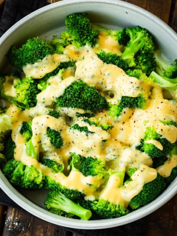 a large bowl of bright green steamed broccoli topped with cheddar cheese sauce and salt and pepper
