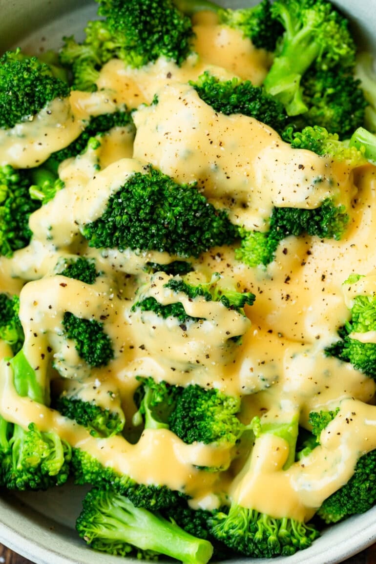Bright green broccoli florets topped with creamy cheddar cheese sauce, salt and pepper