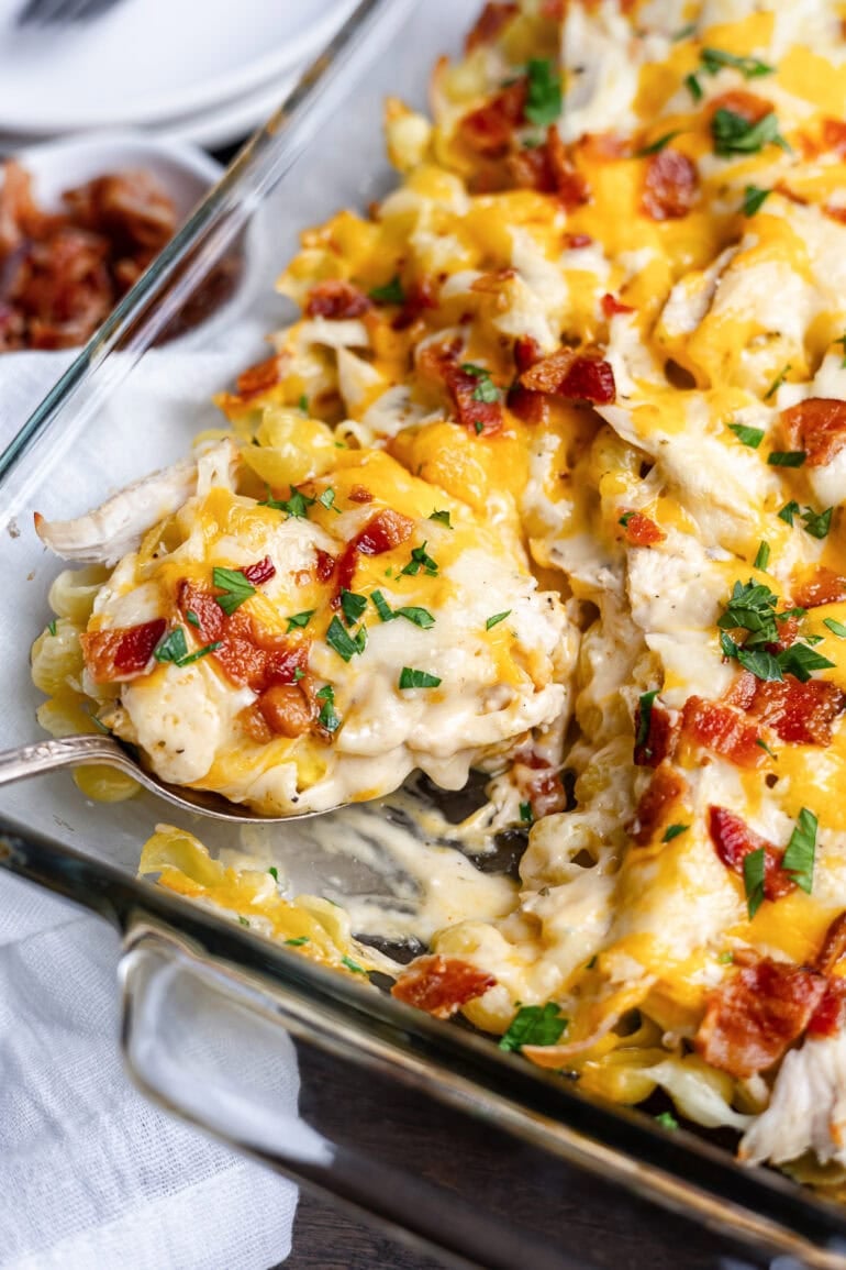 someone scooping a serving of creamy chicken pasta bake from a baking dish