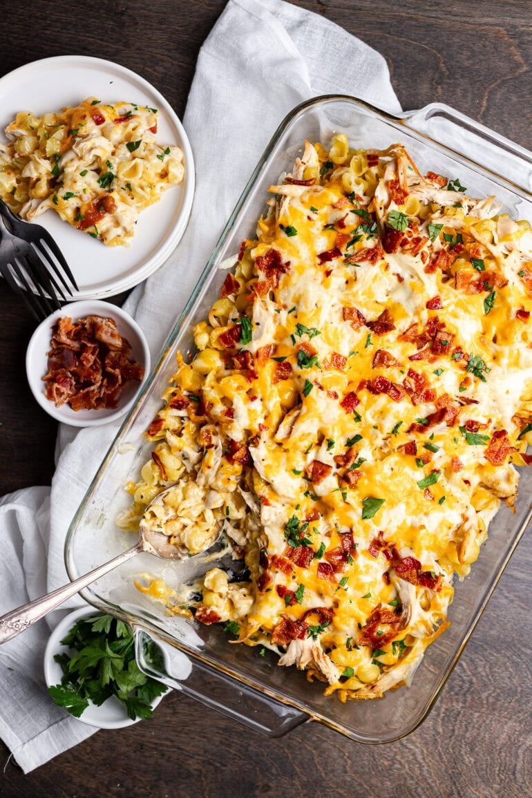 a 9x13 casserole dish full of cheesy chicken bacon ranch casserole with a small bowl of crispy bacon bits on the side