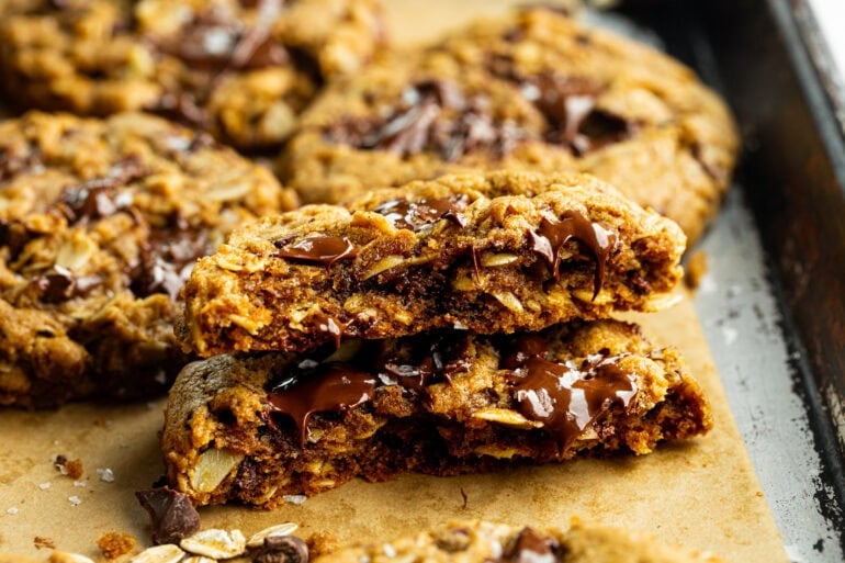 a thick and chewy pumpkin oatmeal cookie that has been broken in half and stacked on each other so you can see the inside of the cookie loaded with melty chocolate chunks