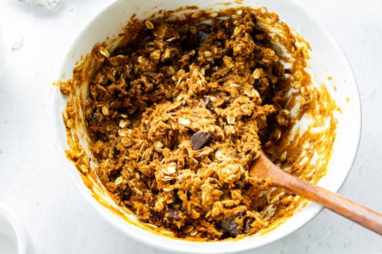 pumpkin oatmeal cookie batter loaded with chocolate chunks being stirred with a wooden spoon