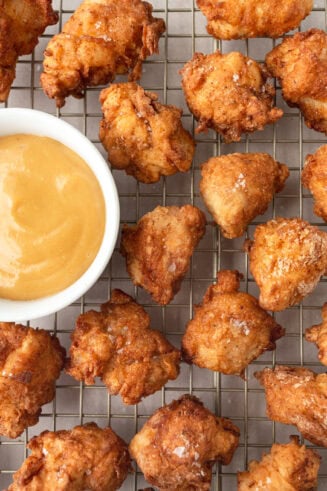 a photo of several homemade chick fil a nuggets sitting on a wire cooling rack with a small bowl of a dipping sauce sitting next to them