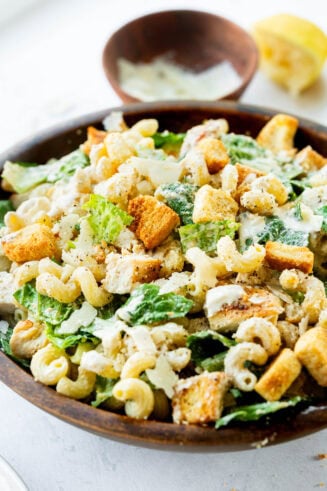 a photo of a large wooden serving bowl full of creamy chicken caesar pasta salad