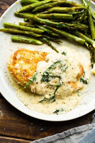 a golden breaded chicken breast covered in a creamy sauce with spinach and a side of asparagus