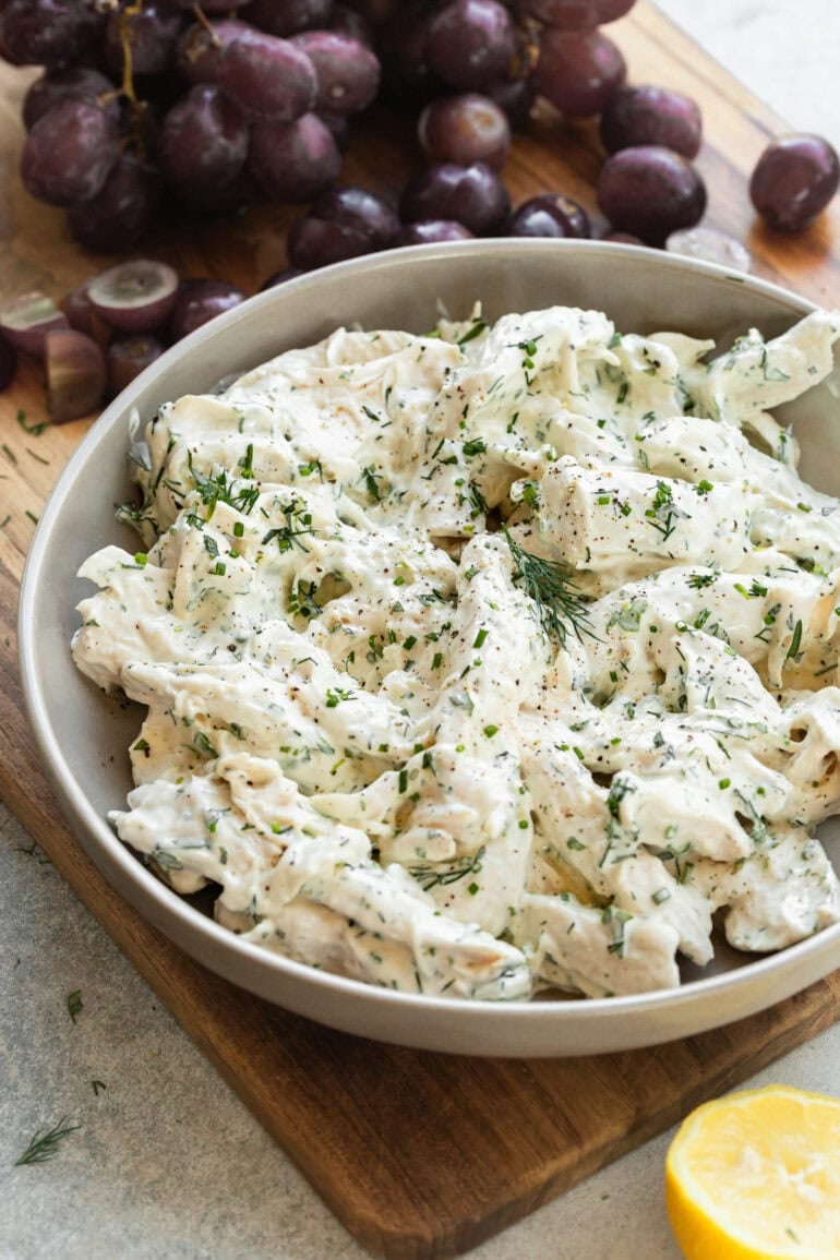 Close-up of shredded chicken salad in a serving bowl with tarragon and dill.