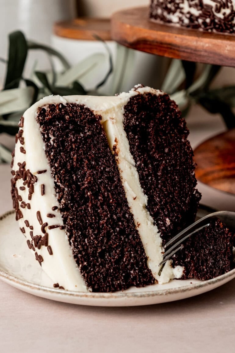 a slice of two layer chocolate cake with vanilla buttercream frosting and chocolate sprinkles with a fork removing a bite from it