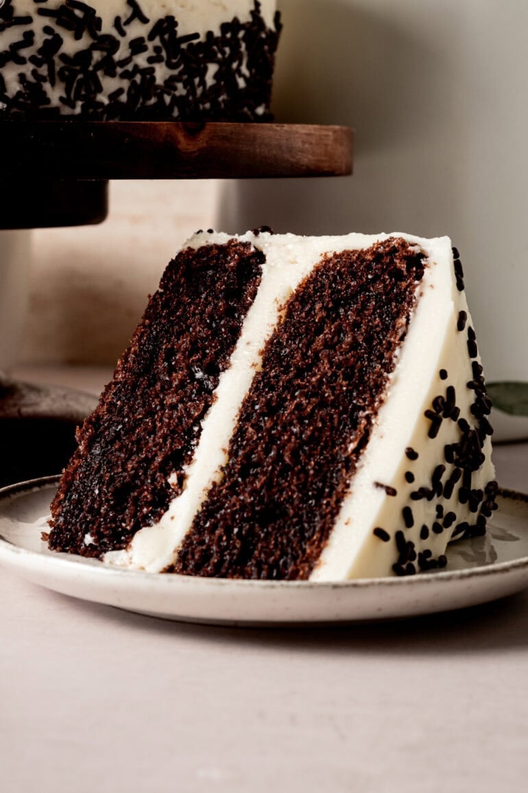 a slice of 2 layer chocolate cake covered and filled with vanilla buttercream frosting and covered with chocolate sprinkles