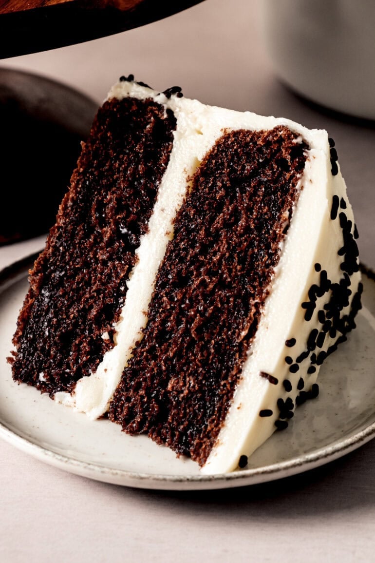 a slice of 2 layer chocolate cake with vanilla buttercream frosting topped with chocolate sprinkles