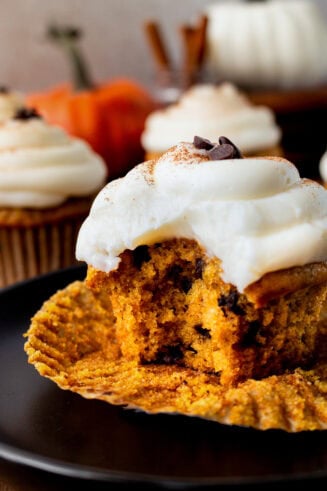 a photo of a chocolate chip pumpkin cupcake with a bite taken out of it and topped with cream cheese frosting