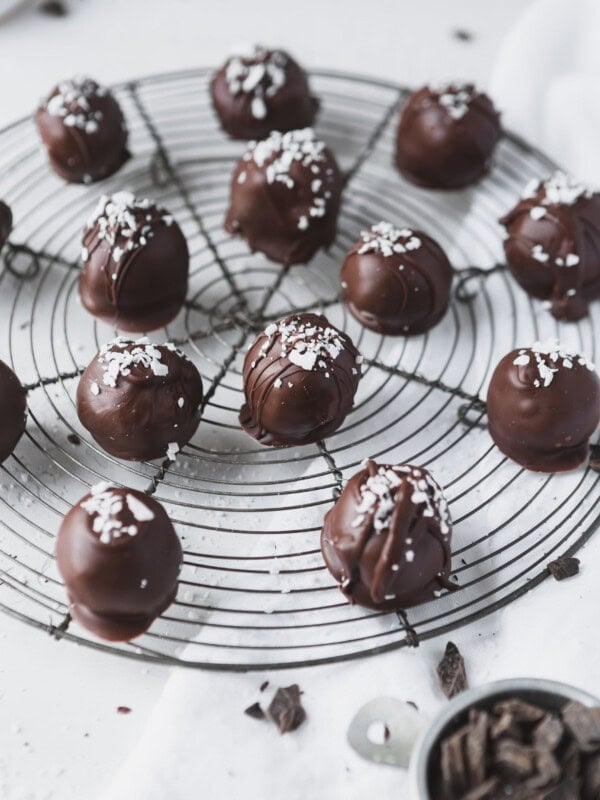 A round wire rack with chocolate dipped coconut balls. A few coconut flakes are sprinkled on top.