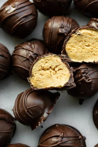 a photo of several dark chocolate covered peanut butter balls with two sliced in half so you can see the peanut butter inside.
