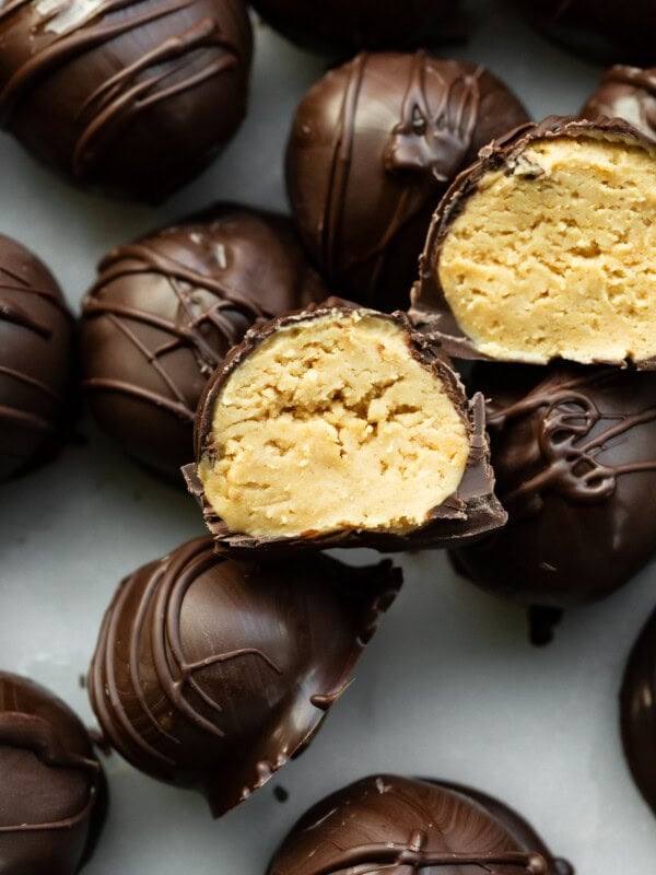 a photo of several dark chocolate covered peanut butter balls with two sliced in half so you can see the peanut butter inside.