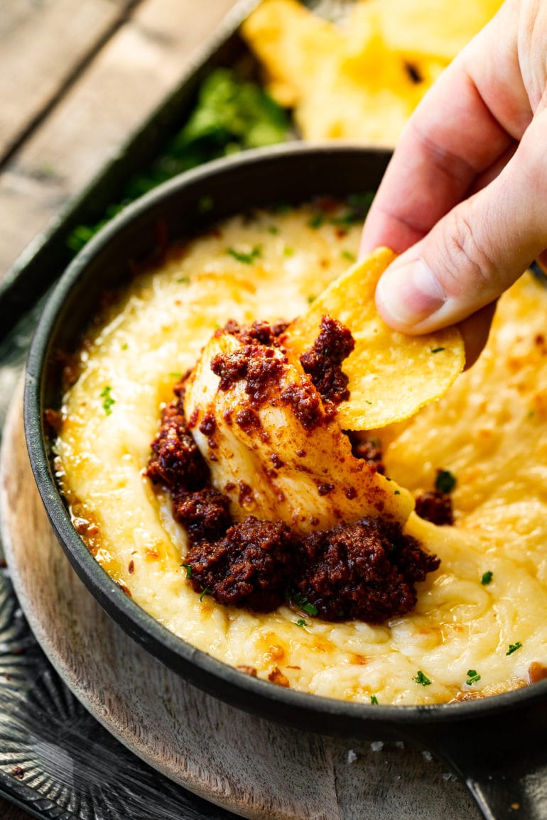 a photo of someone using a tortilla chip to scoop up a big bite of chorizo queso fundido.