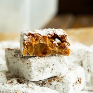 a stack of peanut butter bars coated in powdered sugar with the top bar broken in half so you can see the inside