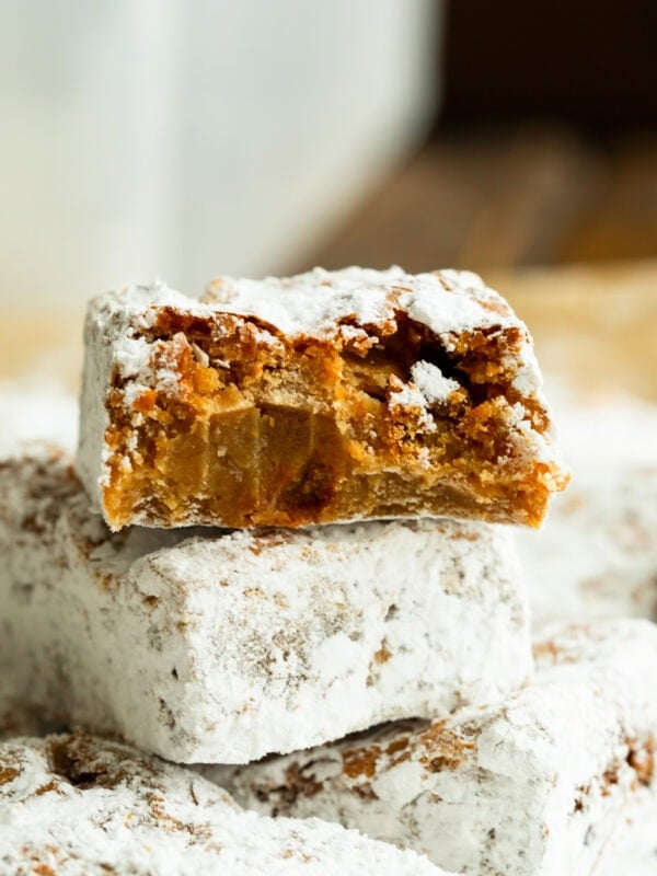 a stack of peanut butter bars coated in powdered sugar with the top bar broken in half so you can see the inside