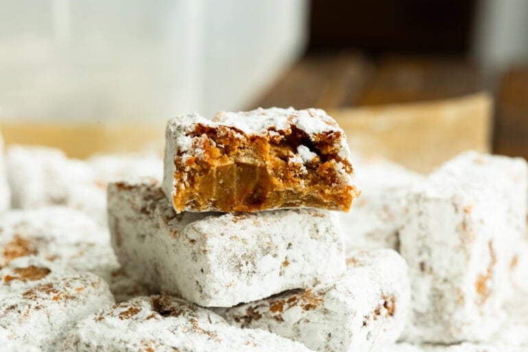 a stack of peanut butter bars coated in powdered sugar with the top bar broken in half so you can see the inside