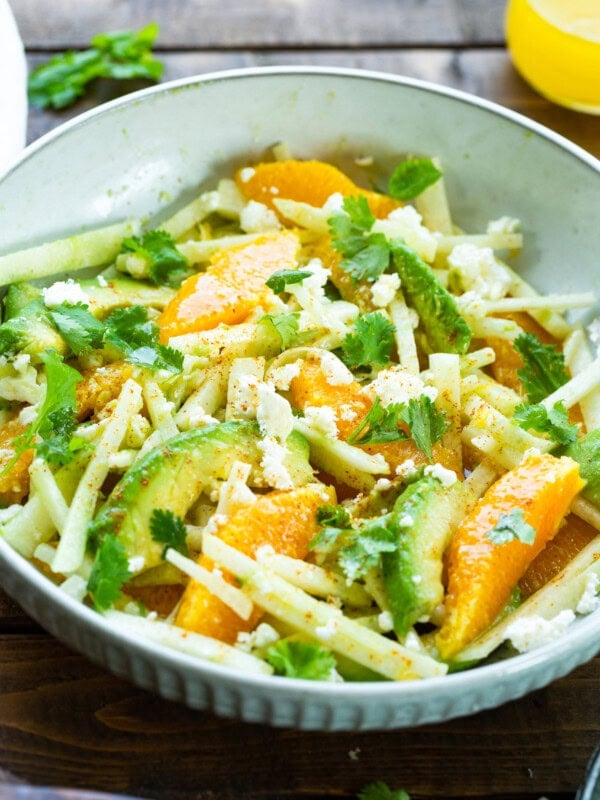 a photo of a large white serving bowl full of sliced orange wedges, sticks of jicama, and slices of ripe avocado.